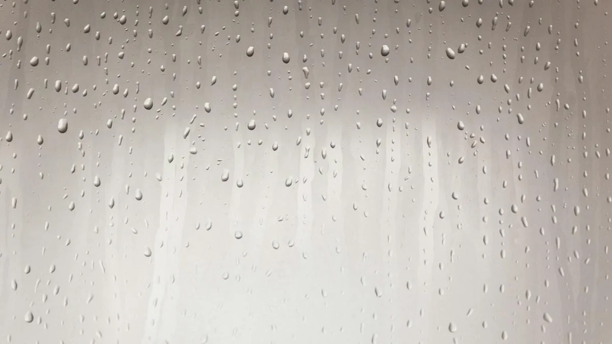 Beads of condensation running down a pale grey surface